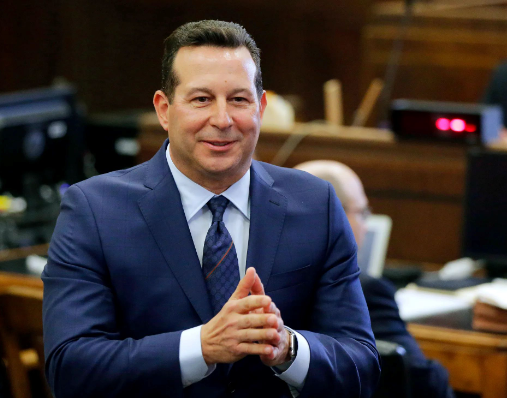 Derek Rosa, in a suit and tie, is standing in a courtroom.